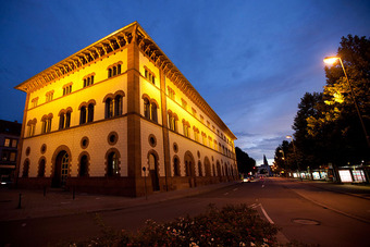 Fruchthalle Kaiserslautern bei Dämmerung, beleuchtet mit warmem Licht, mit Rundbogenfenstern und verzierten Gesimsen.