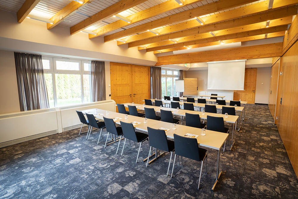 Moderner Konferenzraum mit Holzwänden, großem Tisch, Präsentationsfläche und Tageslicht durch große Fenster.